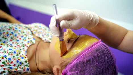 cosmetologist applies alginate mask with spatula on face of woman. facial skin and anti-aging treatment. cosmetology and professional facial skin care.