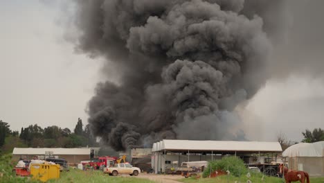 black smoke clouds and flames rise into the sky from burning warehouses in the village.