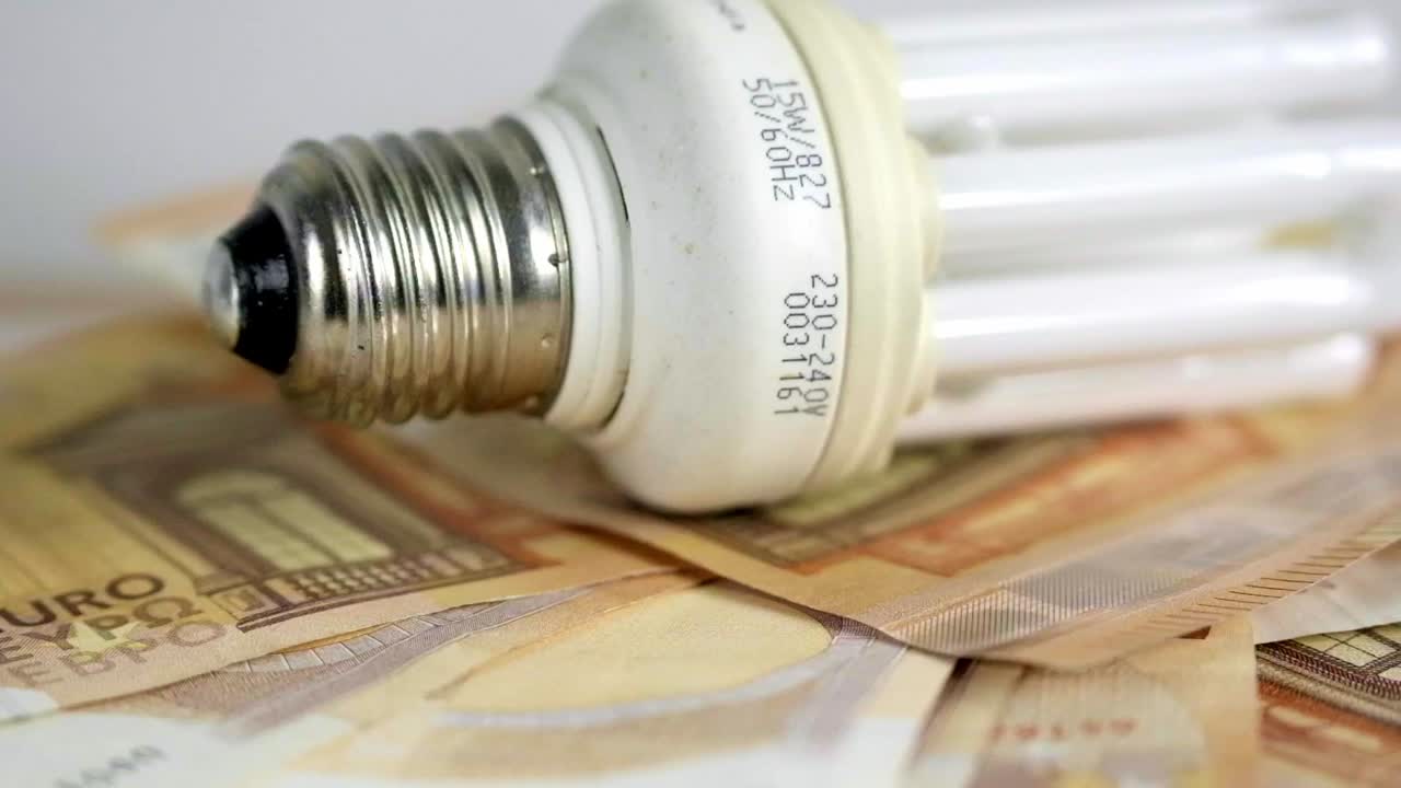 Lampadina che ruota su banconote da 50 euro. Aumento delle tariffe elettriche