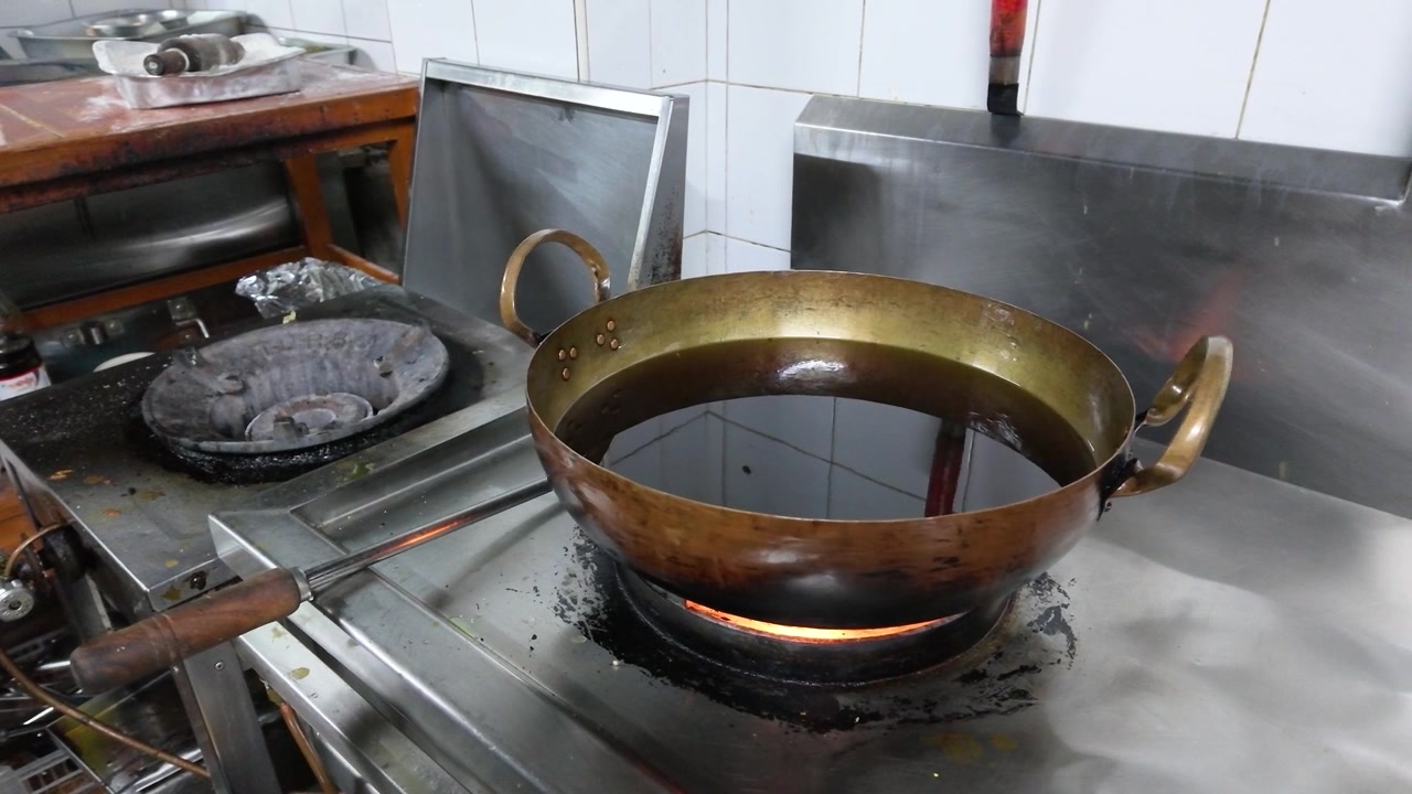 開放されたガス炎の上で油を熱している真鍮製のウォックの固定ミディアムショット