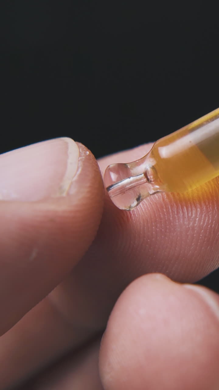 man hand holds glass pipette with light brown liquid on black background extreme close view
