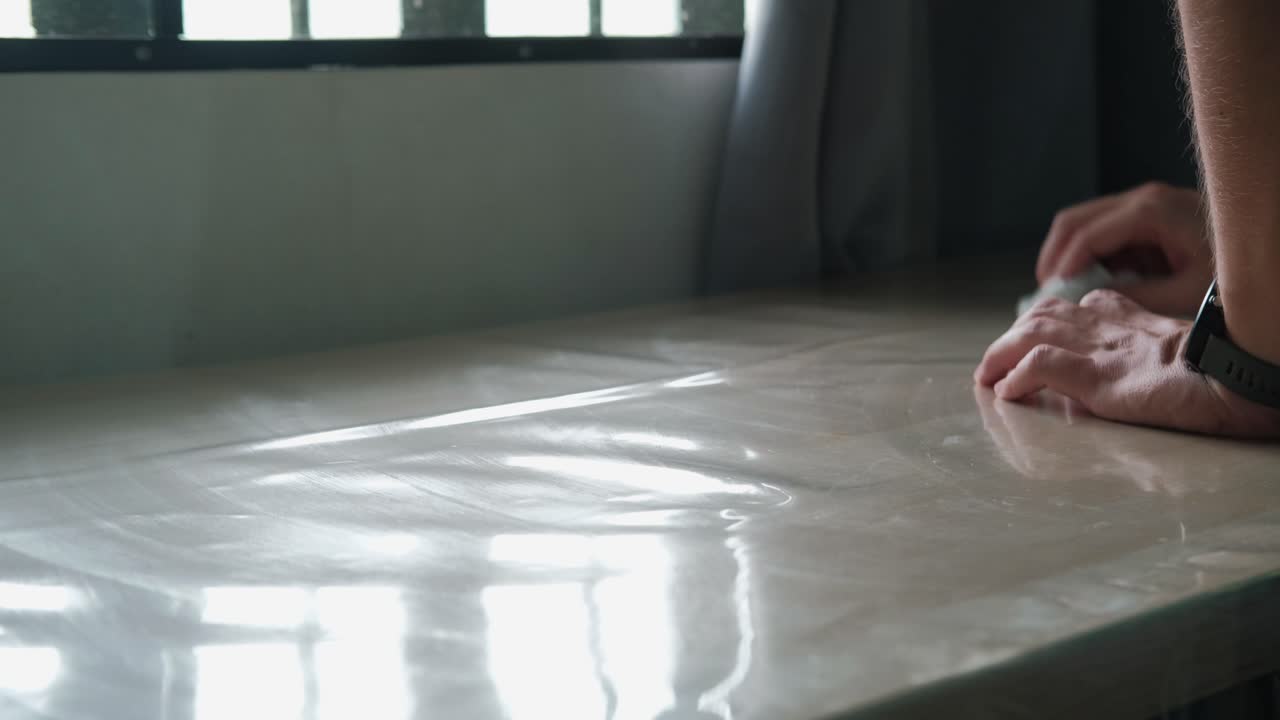 Hands wiping down sunlit kitchen table with paper towel. -static close-up shot