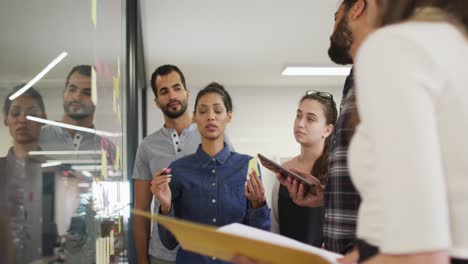 grupo diverso de colegas de trabajo haciendo una lluvia de ideas poniendo notas adhesivas en la pared de vidrio