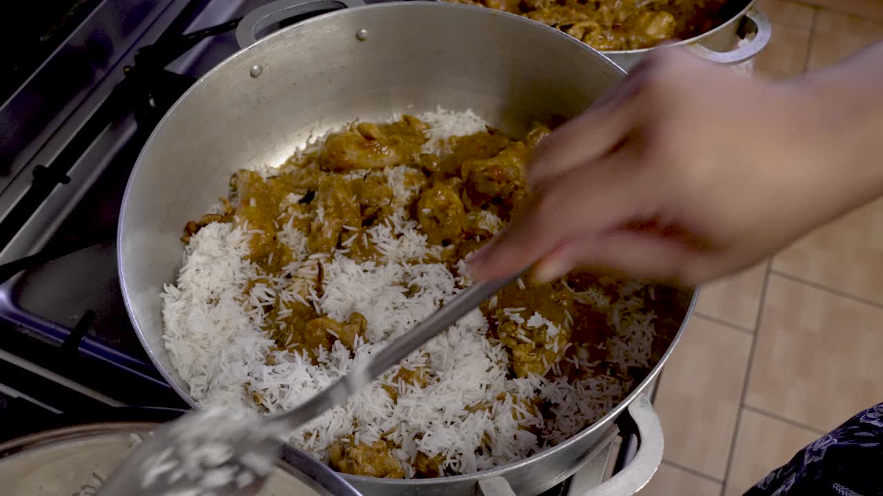 chef agregando arroz blanco a la capa de curry de pollo en una olla grande