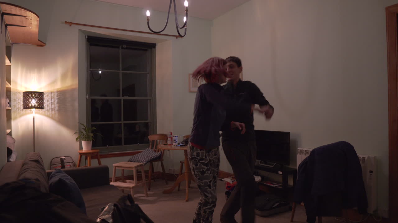 Girl teaching boyfriend how to dance in the middle of a living room at night time with nice and soft warm light.