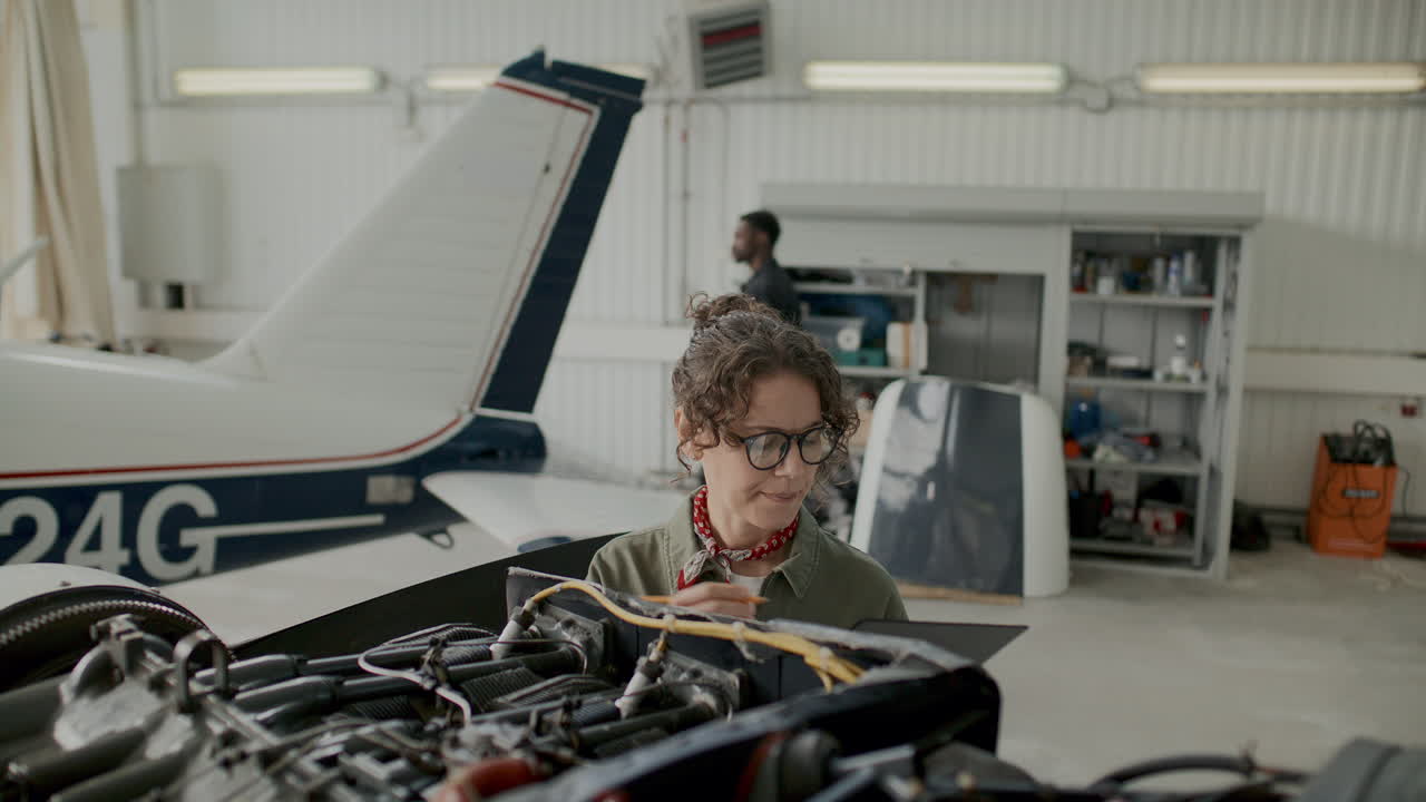 Female Aircraft Technician Checking Engine Parts and Writing Notes in Hangar