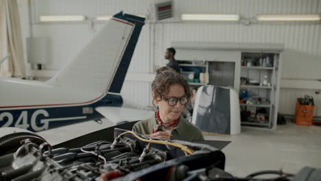female aircraft technician checking engine parts and writing notes in hangar