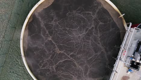 drone footage of circular wastewater treatment tank with aeration, symbolizing purification and environmental care, industrial setting, brown water