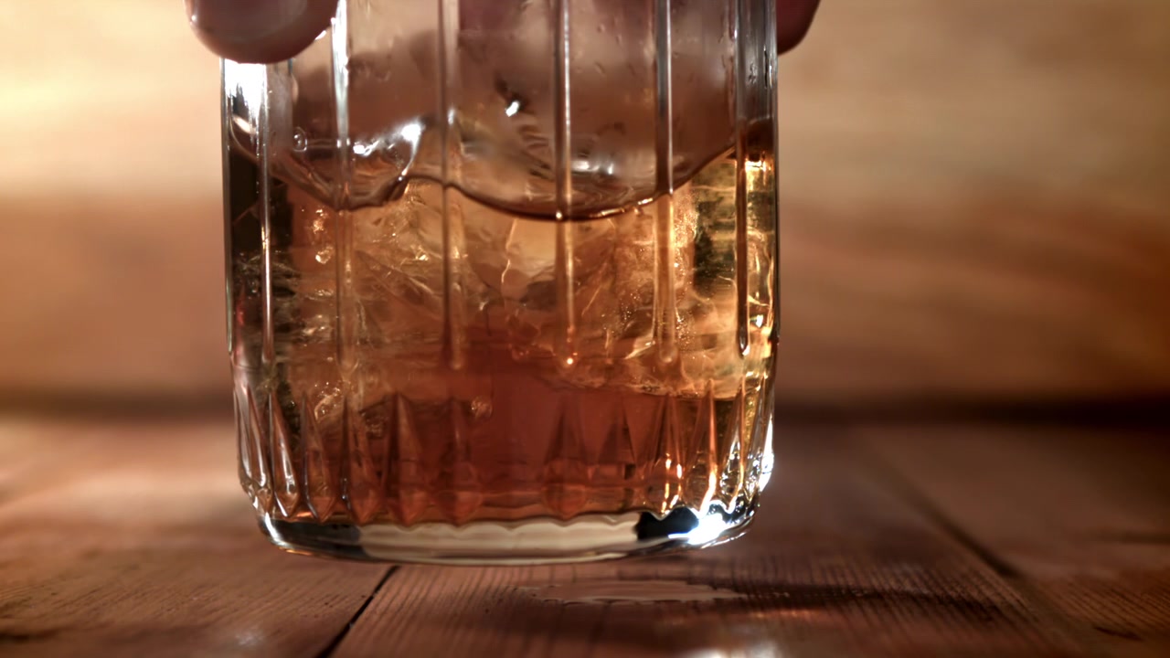 Primo piano al rallentatore di whisky con ghiaccio che turbina in un bicchiere