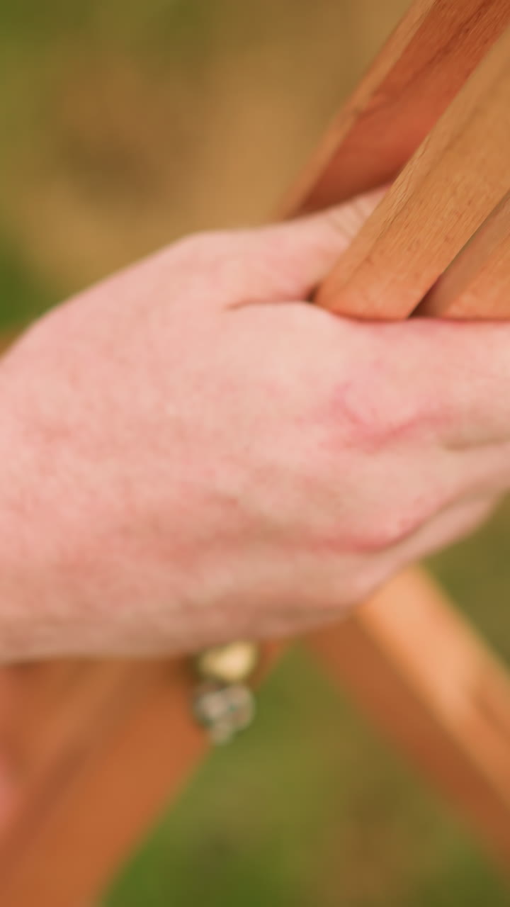 인간 손이 잔디에 나무 삼각대를 조심스럽게 세우는 클로즈업; 주변 지역이 흐릿하여 손과 삼각대에 주의를 집중합니다.