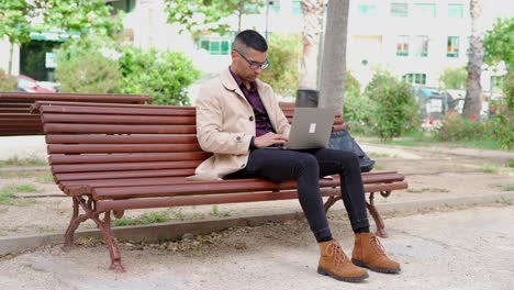 Young-businessman-in-trendy-outfit-speaking-on-phone-on-bench