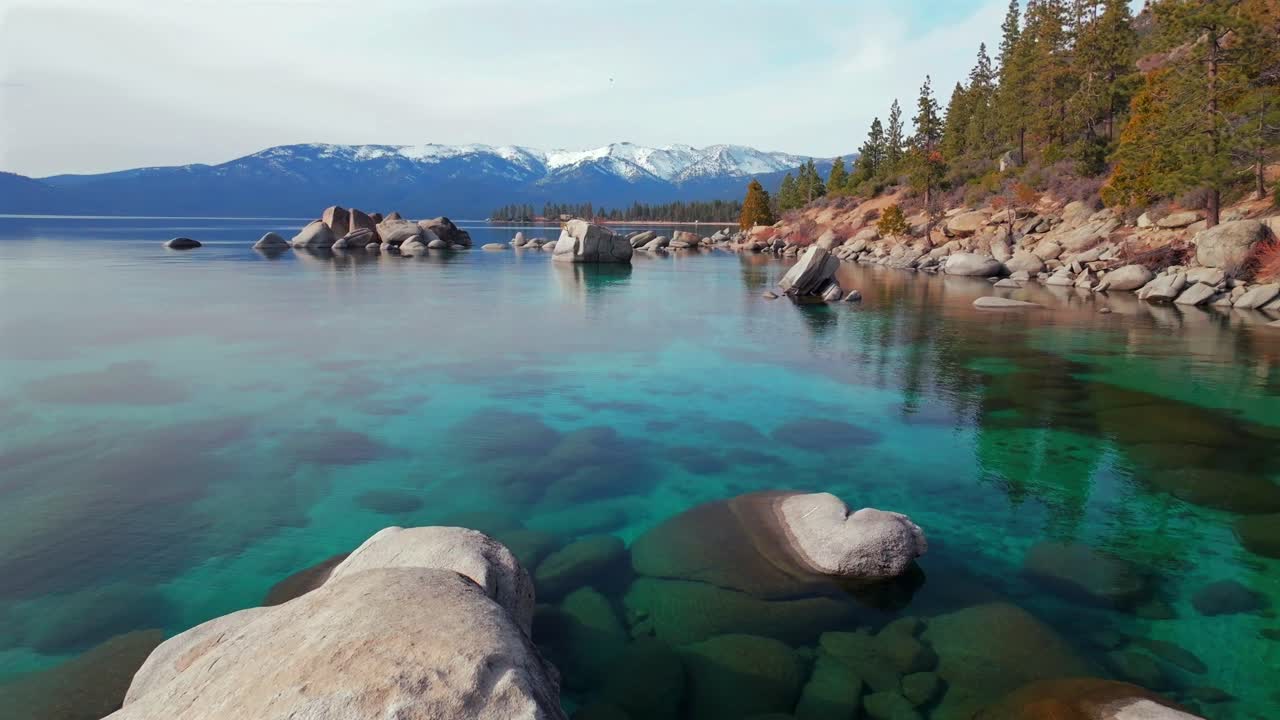Lake Tahoe standing on rocky large boulders shore clear glassy turquoise fresh water aerial drone Sand Harbor California sunny winter clouds Secret Chimney Kings beach Incline Village forward motion