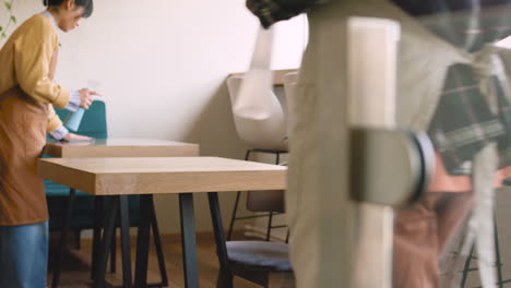 camarera y mesera limpiando la mesa de la cafetería con spray desinfectante y trapo antes de abrir la cafetería