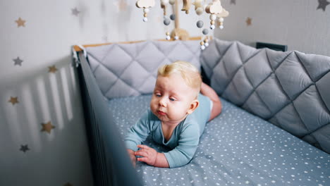 little cute child lying on the belly. adorable infant baby in bodysuit lies in cot under the crib mobile.