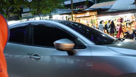 motorcycles and cars pass by a bustling market