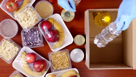 top view, close-up, volunteer in protective gloves packs grocery to cardboard donation box. takeaway, door food delivery service, during coronavirus . shopping online. charity