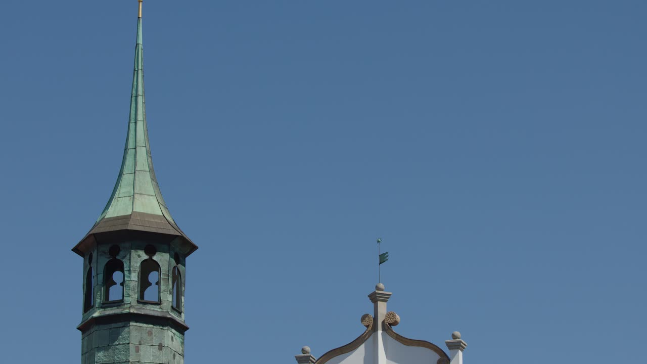 Camera tilts upward revealing ornate Prague architecture and copper spire under clear daylight sky