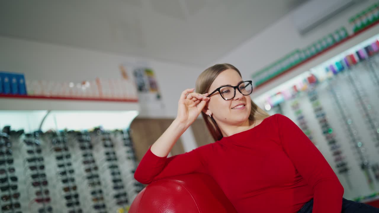 Beautiful woman in stylish eyeglasses. Female customer sitting in armchair and trying on new glasses in optical store. Eyewear concept.