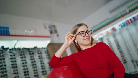 beautiful woman in stylish eyeglasses. female customer sitting in armchair and trying on new glasses in optical store. eyewear concept.
