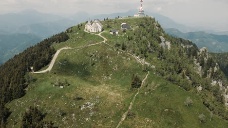 Toma-De-Dron-De-La-Montaña-Uršlja-Tomando-El-Sol,-Cámara-Girando-Hacia-La-Carretera-Que-Conduce-A-La-Cima