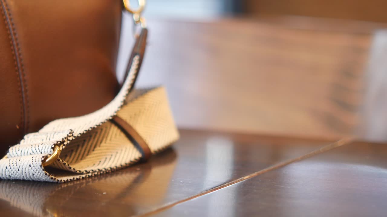 persona sosteniendo un teléfono en una mesa de madera junto a un bolso.