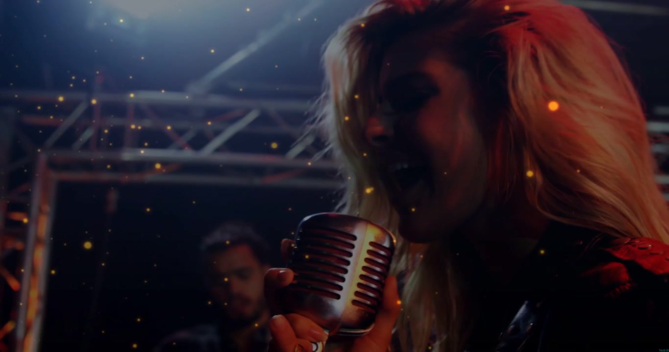 Vertical video: Singer leaning into retro mic, singing music, sparks drifting and guitarist playing