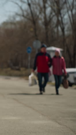 전면에 있는 파란색 공원 벤치의 근접 시각과 배경에 산책하는 사람들, 전기 스쿠터를 타고 있는 검은색 옷을 입은 사람의 흐릿한 시각