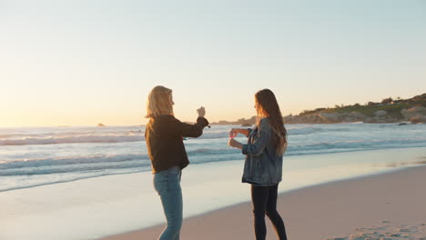 Freundinnen-Blasen-Am-Strand-Bei-Sonnenuntergang-Seifenblasen-Und-Haben-Spaß-Im-Sommer,-Spielen-Am-Meer-Und-Genießen-Die-Freundschaft