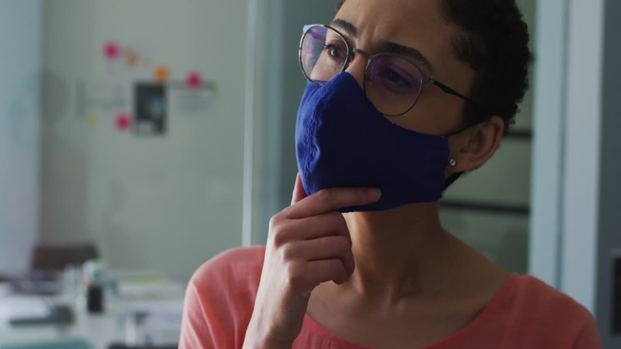 Donna caucasica pensierosa con mascherina e mano sul mento in un ufficio moderno