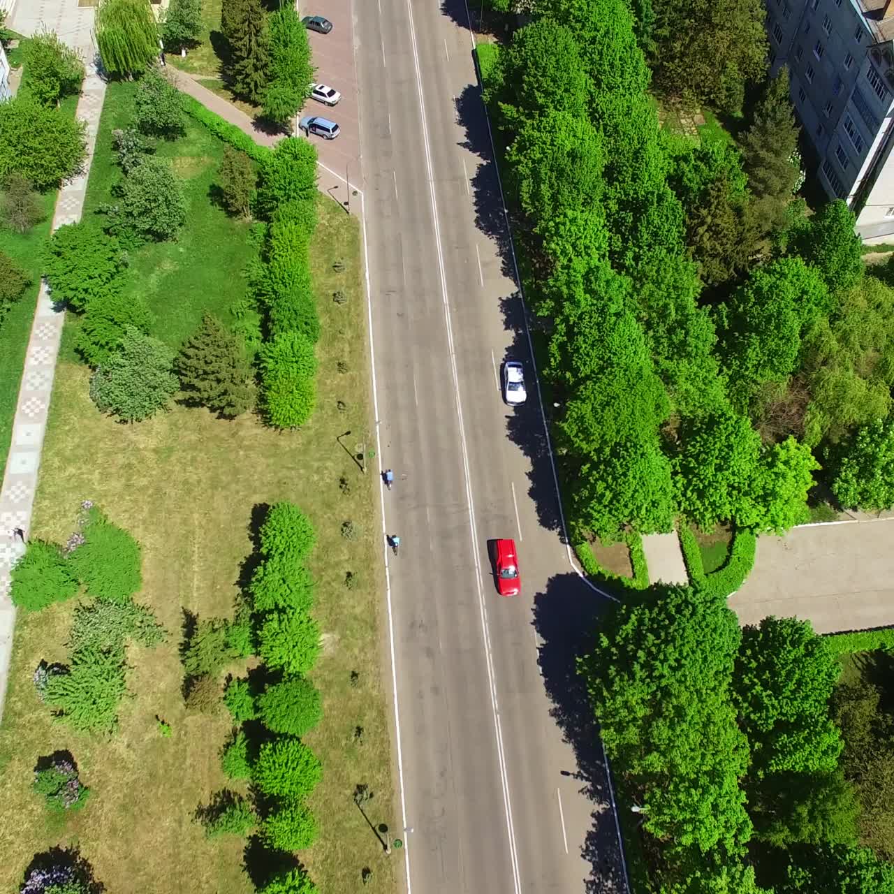 Few cars moving by the empty road through residential area. Multi-storied buildings, cottages and lots of greenery in the outskirts of the town. Top view