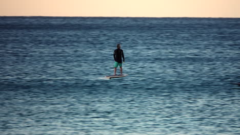 middle age man in green shorts riding an electric foil board on the ocean at sunset.