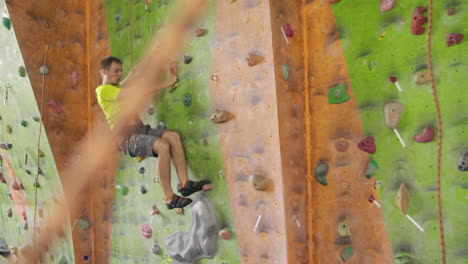 climber moves on the mountain in a room with a rope on the insurance and a bag for chalk overcoming the height rises to the top in slow motion.