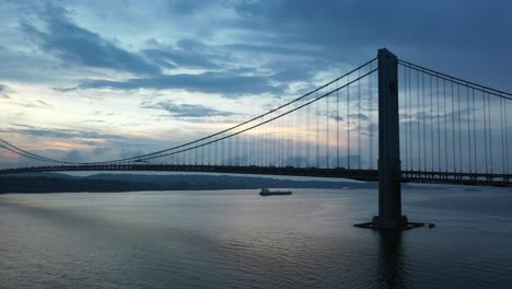 an aerial view over gravesend bay in brooklyn, ny. the drone camera slowly dolly out from the verrazzano bridge and a lone cargo ship. it was taken during a cloudy sunset
