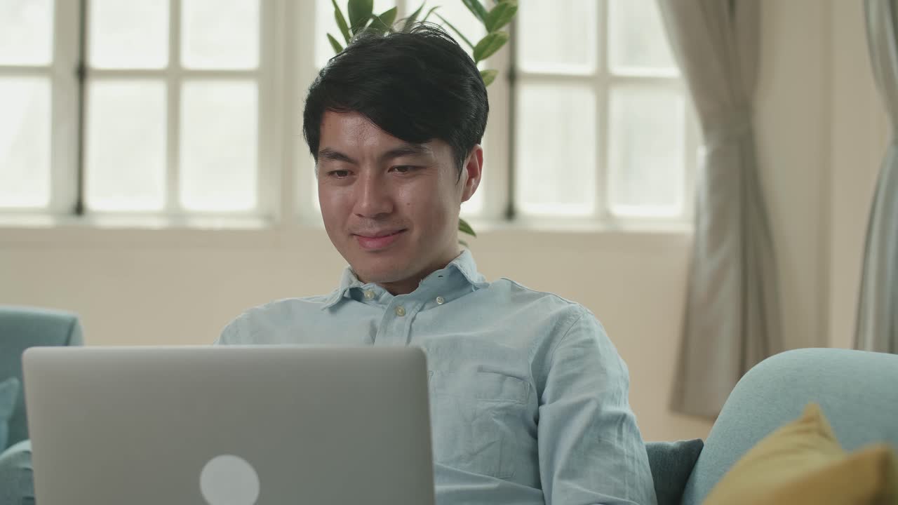 Asian Male Use Laptop Computer In Living Room While Lying On Sofa, Video In 4K