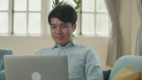 asian male use laptop computer in living room while lying on sofa, video in 4k