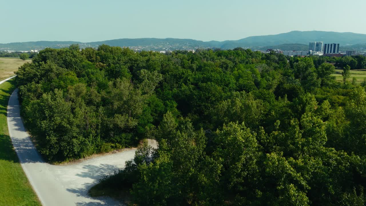 drone shows curved white path beside green trees near Zagreb with cityscape in background