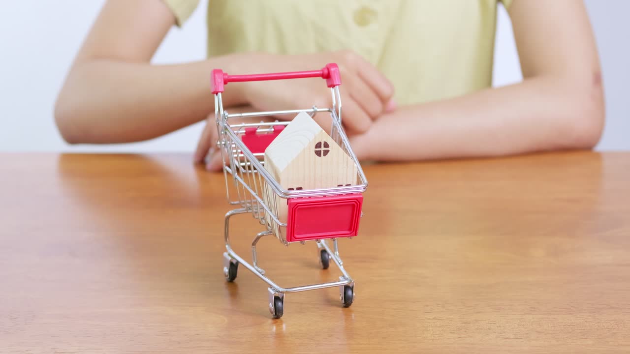 A creative representation of purchasing a home showcasing a house on a shopping cart