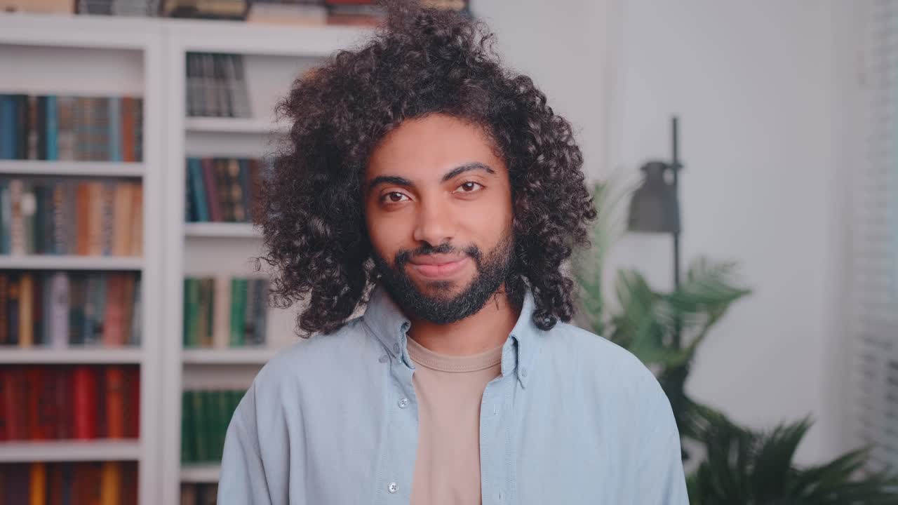 Young arabian man smiling and laughing looking at camera stands in library