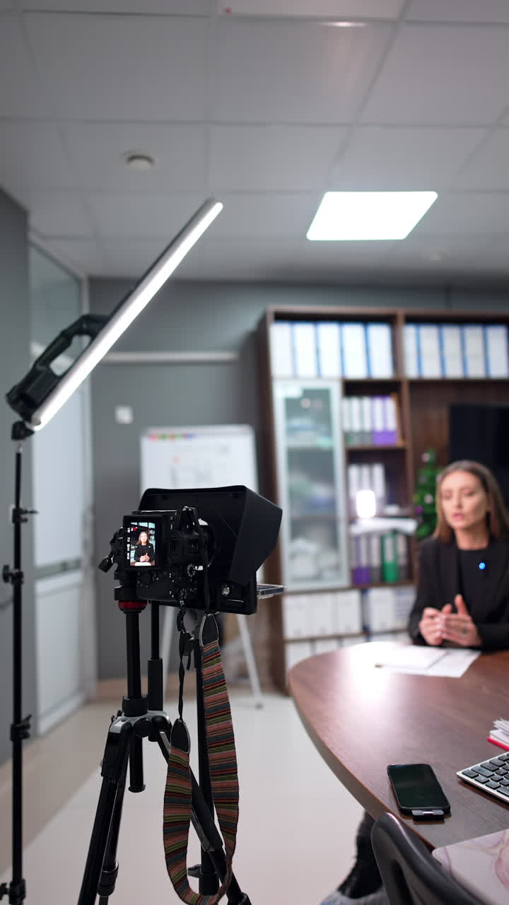 Beautiful woman recording video in the office sitting at desk. Pedagogue filming content for educational blog. Vertical video.