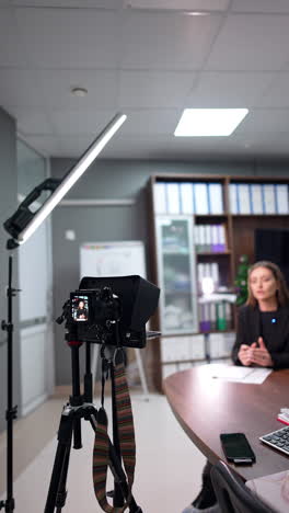 beautiful woman recording video in the office sitting at desk. pedagogue filming content for educational blog. vertical video.