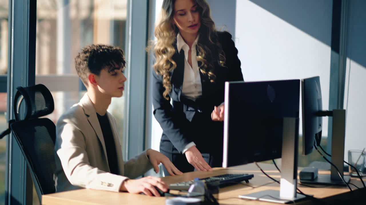 Female team leader discussing business affairs with a young worker which is working in a computer. Business meeting at the office