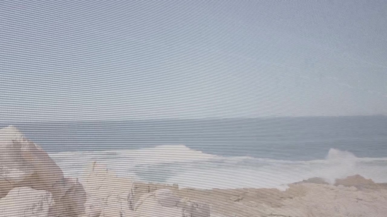 Swell cresting causing panning left waves breaking foam sliding trail fading scanline showing coast