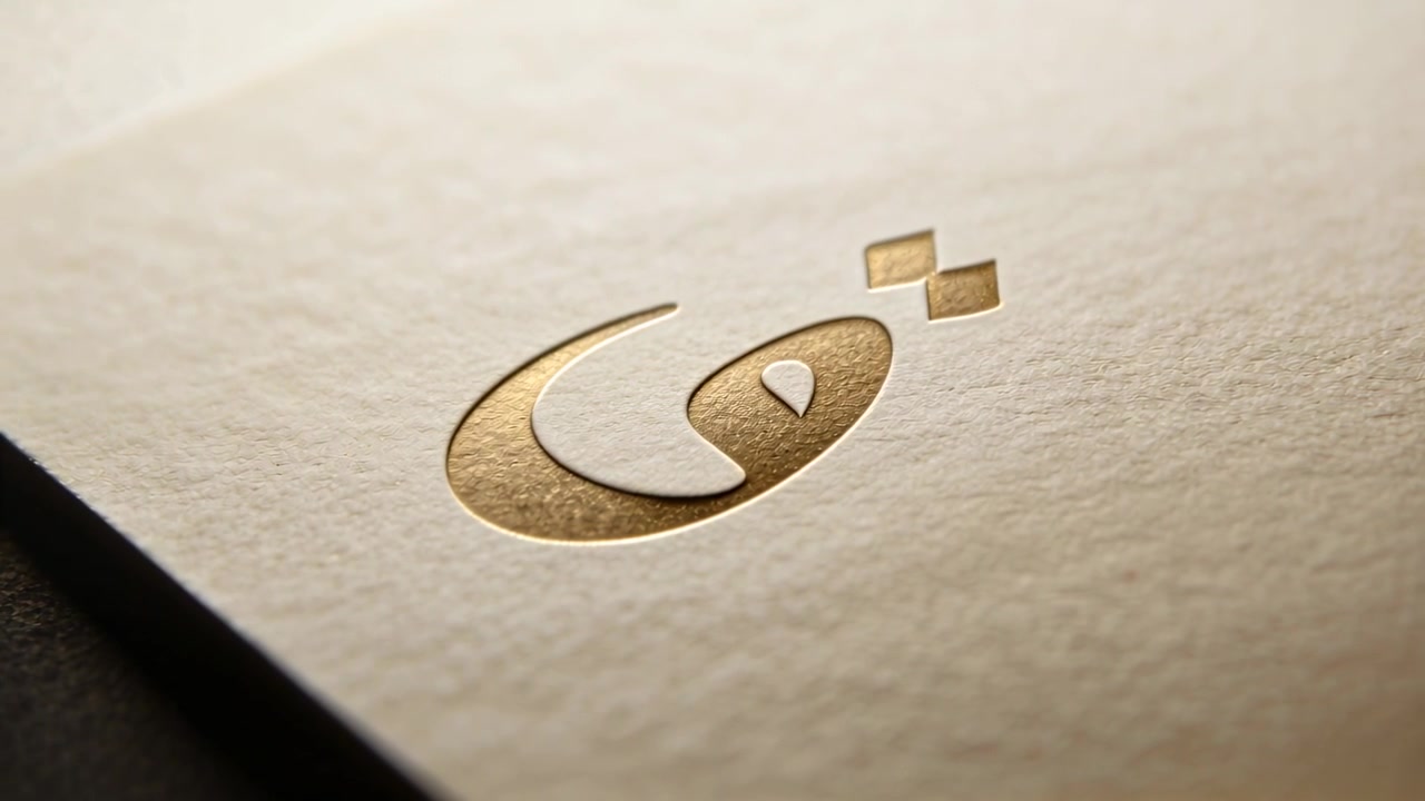 Panning camera revealing gold debossed logo with gold squares on cream paper, emphasizing texture