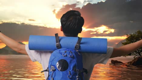 close up back view of a male hiker with mountaineering backpack spreading arms and looking the view around at a lake