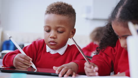 Ein-Junge-Und-Ein-Mädchen-Benutzen-Einen-Tablet-Computer-Und-Einen-Stift-An-Einem-Schreibtisch-In-Einem-Klassenzimmer-Einer-Kleinkinderschule,-Rack-Fokus