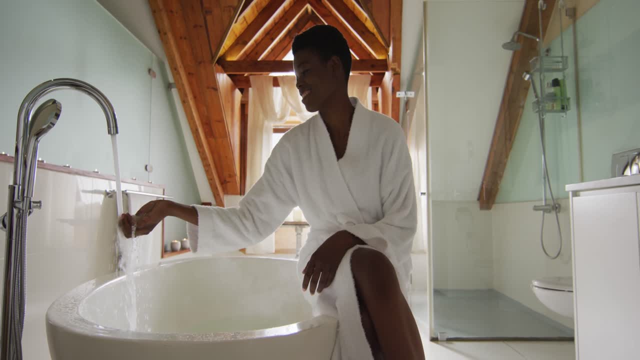 Smiling african american attractive woman in white robe sitting on bathtub, preparing bath