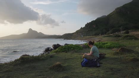 mujer sentada en la playa rocosa leyendo un libro en kindle en la isla de con dao, vietnam