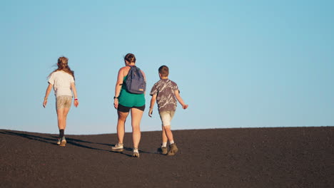 three hikers ascend a dark hill under a clear blue sky