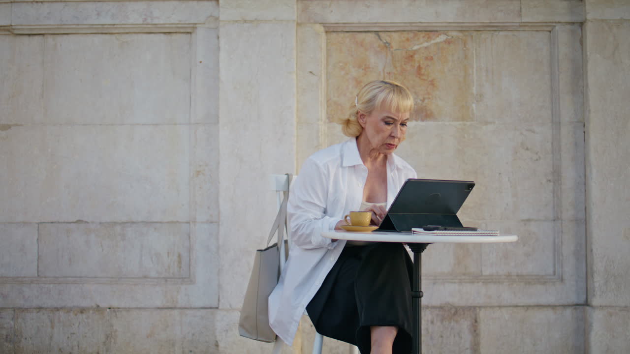 Retired manager working remotely at street cafe. Mature woman typing laptop