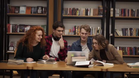 Gruppe-Junger-Studenten,-Die-Sich-Mit-Einem-Laptop-Unterhalten-Und-Die-Kursarbeit-Erklären,-Lernen-Gemeinsam-In-Bibliothek-1